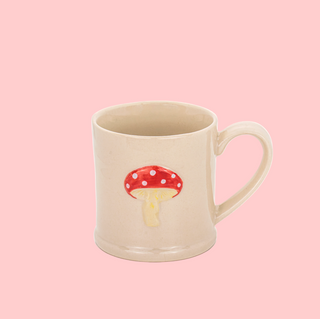 Beige mug with a red mushroom design on a white background